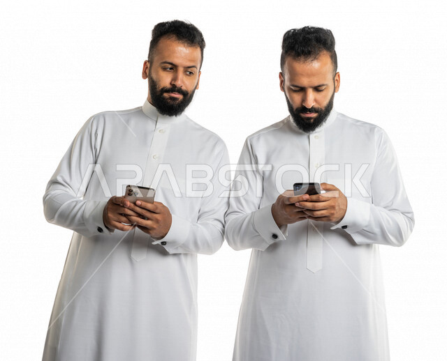 بورتريه لرجلان توأم عربيان خليجيان سعوديان يستخدمان الهاتف المحمول ، النظر خلسة للهاتف الاخر ، المراقبة والتطفل ، التلصص على الهواتف الشخصية،ادمان الانترنت ، خلفية بيضاء