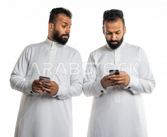 بورتريه لرجلان توأم عربيان خليجيان سعوديان يستخدمان الهاتف المحمول ، النظر خلسة للهاتف الاخر ، المراقبة والتطفل ، التلصص على الهواتف الشخصية،ادمان الانترنت ، خلفية بيضاء