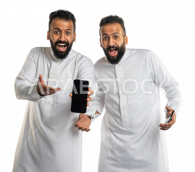 بورتريه لرجلان توأم عربيان خليجيان سعوديان يعرضان الهاتف المحمول ببهجة وحماس ، استخدام البرامج والتطبيقات الالكترونية ، الإعلانات التسويقية ، اعلانات تجارية ، عروض ترويجية ، دعاية و اعلان ، التسويق و الاعلانات