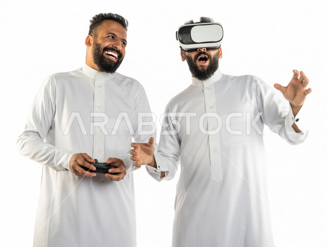 بورتريه لرجلان توأم عربيان خليجيان سعوديان احدهم يرتدي نظارة الواقع الافتراضي والاخر يمسك بيده عصا التحكم، نظارة الواقع الافتراضي، نظارة ثلاثية الابعاد، عصا التحكم، ألعاب الفيديو، المتعة والتسلية، العالم الافتراضي، خلفية بيضاء