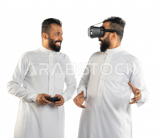 بورتريه لرجلان توأم عربيان خليجيان سعوديان احدهم يرتدي نظارة الواقع الافتراضي والاخر يمسك بيده عصا التحكم، نظارة الواقع الافتراضي، نظارة ثلاثية الابعاد، عصا التحكم، ألعاب الفيديو، المتعة والتسلية، العالم الافتراضي، خلفية بيضاء