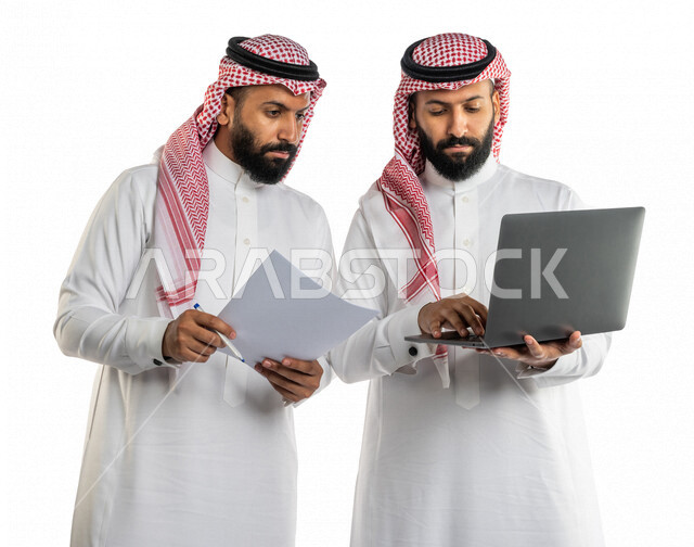 بورتريه لرجلان توأم عربيان خليجيان سعوديان يتنقاشان في مهام العمل، اجتماع زملاء العمل في مقر عملهم، استخدام الحاسوب المحمول في تطوير العمل وحل المشكلات، توزيع مهام العمل، الوحده والعمل الجماعي، بيئة عمل سعودية، استخدام تقنيات حديثة، خلفية بيضاء