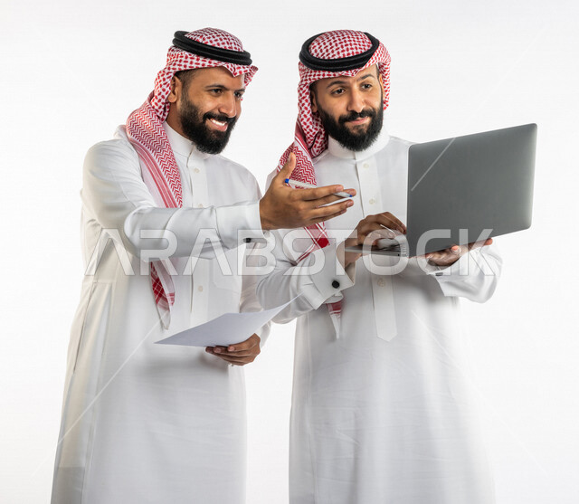 بورتريه لرجلان توأم عربيان خليجيان سعوديان يتنقاشان في مهام العمل، اجتماع زملاء العمل في مقر عملهم، استخدام الحاسوب المحمول في تطوير العمل وحل المشكلات، توزيع مهام العمل، الوحده والعمل الجماعي، بيئة عمل سعودية، استخدام تقنيات حديثة، خلفية بيضاء