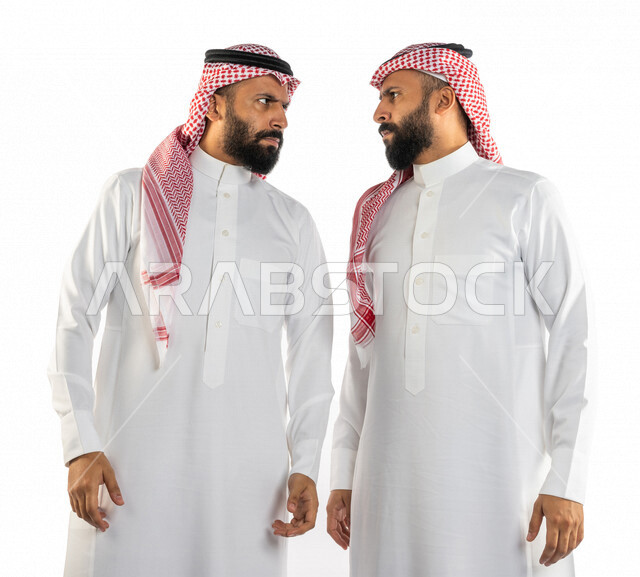 بورتريه لرجلان توأم عربيان خليجيان سعوديان يقفان مقابل بعضهم، نقاش حاد بين اخوين توأم، الغضب والقاء اللوم، النقاش والمواجهة، السؤال والاستفسار عن شيء ما، التهيج والتوتر، الضغط العصبي، ايماءات وجه ويدين تدل على الغضب، خلفية بيضاء