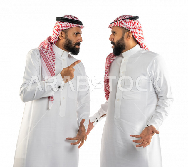 بورتريه لرجلان توأم عربيان خليجيان سعوديان يقفان مقابل بعضهم، نقاش حاد بين اخوين توأم، الغضب والقاء اللوم، النقاش والمواجهة، السؤال والاستفسار عن شيء ما، التهيج والتوتر، الضغط العصبي، ايماءات وجه ويدين تدل على الغضب، خلفية بيضاء