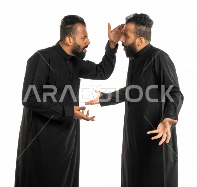 بورتريه لرجلان توأم عربيان خليجيان سعوديان يقفان مقابل بعضهم، نقاش حاد بين اخوين توأم، الغضب والقاء اللوم، النقاش والمواجهة، السؤال والاستفسار عن شيء ما، التهيج والتوتر، الضغط العصبي، ايماءات وجه ويدين تدل على الغضب، خلفية بيضاء