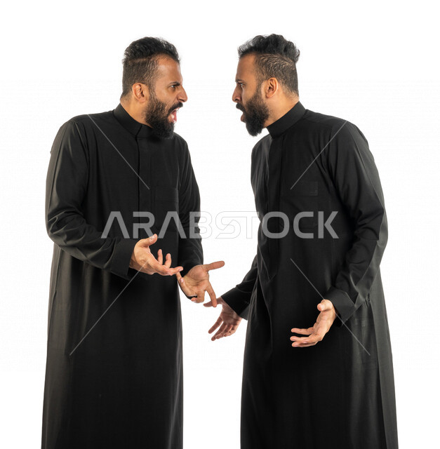 بورتريه لرجلان توأم عربيان خليجيان سعوديان يقفان مقابل بعضهم، نقاش حاد بين اخوين توأم، الغضب والقاء اللوم، النقاش والمواجهة، السؤال والاستفسار عن شيء ما، التهيج والتوتر، الضغط العصبي، ايماءات وجه ويدين تدل على الغضب، خلفية بيضاء