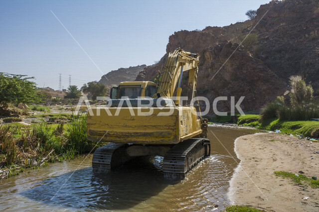 صورة لحفارة هيدروليكية في نهر ، أداة حفر هندسية ، معدات ثقيلة لأعمال انشائية ، آلة حفر و هدم و جر ، جرف الأرض ، محرك طاقة كبير