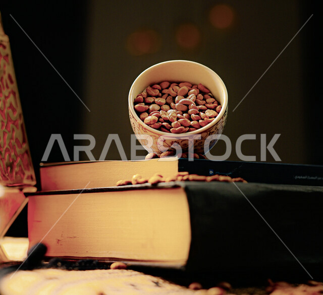 صورة جمالية مقربة لفنجان قهوة مزخرف يحتوي على حبوب البن فوق مجموعة من الكتب ، حبوب القهوة البنية المتناثرة على الكتب ، الاستمتاع بالقهوة و قراءة الكتب 