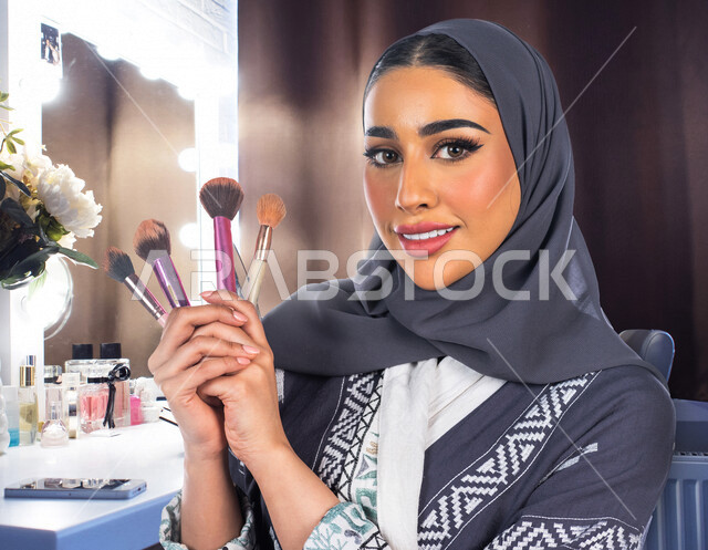 مرأة عربية خليجية سعودية محجبة، تحمل مجموعة من فرش المكياج إحدى أدوات التجميل على بشرة الوجه، مرأة خبيرة بمستحضرات التجميل، التسويق لمنتجات التجميل، متجر بيع مستحضرات التجميل، مفهوم الإهتمام بالجمال والبشرة، ادوات مكياج تتوريال، صالون تجميلي نسائي