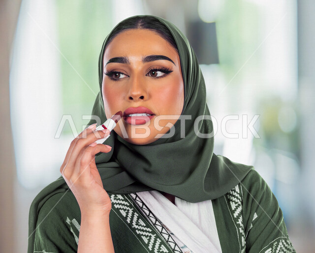 صورة مقربة لمرأة عربية خليجية سعودية محجبة، تحمل إحدى أدوات التجميل (قلم أحمر الشفاة)، مرأة خبيرة بمستحضرات التجميل، التسويق لمنتجات التجميل، متجر بيع مستحضرات التجميل عبر الإنترنت، مفهوم الإهتمام بالجمال والبشرة، ادوات مكياج تتوريال، خلفية ضبابية