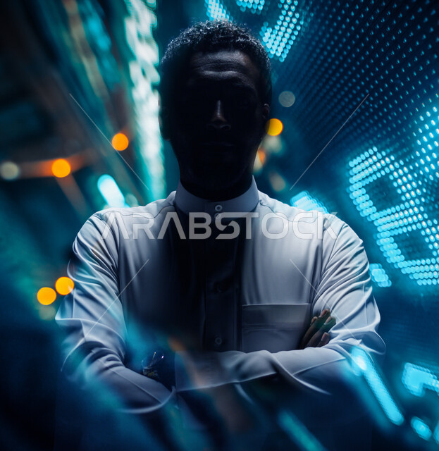 صورة مقربة لرجل عربي سعودي خليجي يرتدي الثوب السعودي ، يقف بإستقامه ، بإيدي متقاطعة ، ينظر إلى الكاميرا ، الوقوف بثقه ، ملامح مخفية ضبابية ، خلفية لبيانات رقمية بتقنية الهولوجرام ثلاثية الأبعاد