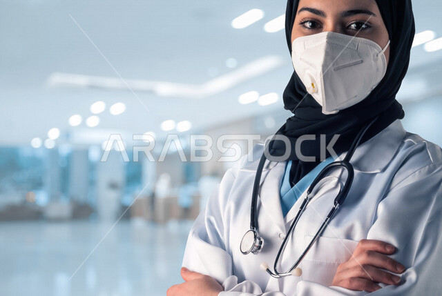 طبيبة عربية خليجية سعودية ترتدي الكمامة الواقية، مفهوم الطب والرعاية الصحية، تقديم الخدمات الطبية للمرضى، إيماءات وجه ويدين مختلفة الوقوف بإستقامة، يدان متقاطعتان، الوقوف بثقة