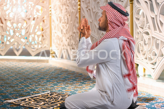 رجل عربي سعودي خليجي يرفع يديه لاعلى للدعاء والتضرع الى الله اثناء الصلاة ، العبادة والتقرب الى الله  ، الصلاة و التسبيح ، أذكار وأدعية ، خلفية داخل المسجد