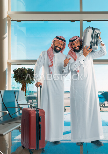 رجلان توأم عربيان خليجيان سعوديان مبتسمان وسعيدان ، يحملان حقائب السفر داخل قاعة الانتظار في المطار ، الاستعداد للسفر، رحلة سياحية ، رحلة عمل ، قضاء وقت ممتع ، الاستعداد لقضاء العطلة الصيفية 