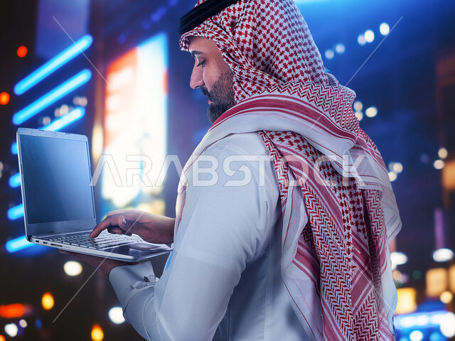 رجل أعمال عربي سعودي خليجي يستخدم جهاز الابتوب، رسوم بيانية إحصائية للبورصة المالية بتقنية الهولوجرام ثلاثية الأبعاد، تطوير الشركات والمشاريع الاقتصادية، التجاره الإلكترونيه، متابعة الأسهم، الإستثمار المالي