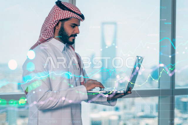 رجل أعمال عربي سعودي خليجي يستخدم جهاز الابتوب، رسوم بيانية إحصائية للبورصة المالية بتقنية الهولوجرام ثلاثية الأبعاد، تطوير الشركات والمشاريع الاقتصادية، التجاره الإلكترونيه، متابعة الأسهم، الإستثمار المالي