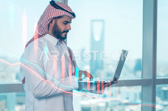 رجل أعمال عربي سعودي خليجي يستخدم جهاز الابتوب، رسوم بيانية إحصائية للبورصة المالية بتقنية الهولوجرام ثلاثية الأبعاد، تطوير الشركات والمشاريع الاقتصادية، التجاره الإلكترونيه، متابعة الأسهم، الإستثمار المالي
