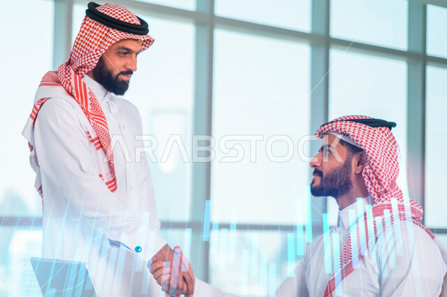 رجلان عربيان سعوديان خليجيان يتصافحان في مقر العمل، اتفاقية عمل, مشروع وخطة عمل جديده, نجاح صفقة عمل, رسوم بيانية للبورصة المالية بتقنية الهولوجرام ثلاثية الأبعاد، متابعة الأسهم، الإستثمار المالي, صفقات تجاريه 
