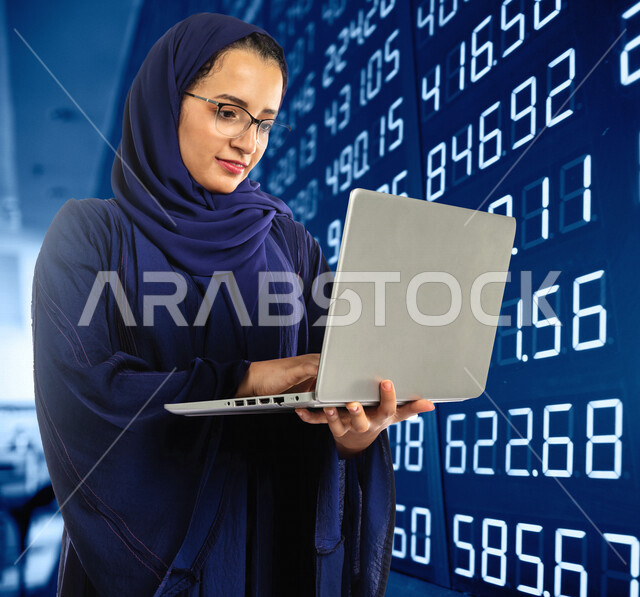 إمرأه عربيه سعوديه خليجيه تستخدم جهاز الحاسوب، متابعة سوق الاوراق الماليه, التجاره الإلكترونيه, مراقبة الإقتصاد والمعلومات الماليه, البورصه, خلفيه مضيئه للوحة البورصه الرقميه