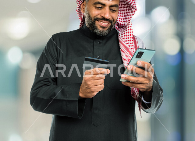 رجل عربي سعودي خليجي يستخدم الهاتف المحمول، استخدام بطاقة الصراف للدفع الإلكتروني, التسوق عبر الإنترنت, التجاره الإلكترونيه، الإستثمار المالي, طلبات الأونلاين, الدفع عن طريق بطاقة الإئتمان, الشراء عبر برامج وتطبيقات الهاتف المحمول