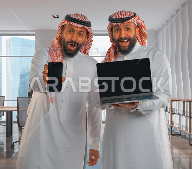 Two Saudi Arabian Gulf twin men at the company’s headquarters, electronic software and applications, advertising and promotion, displaying web pages, e-marketing, facial gestures indicating happiness and surprise, hollow black laptop screen, hollow black 
