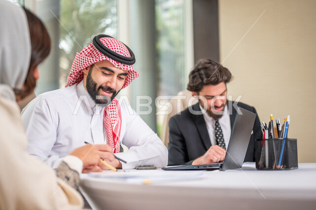 A Saudi Arabian Gulf team in a business meeting with a new client wearing a formal suit, using a laptop computer in developing work and solving problems, developing projects, studying and analyzing new projects, evaluating partnership work, partnership an