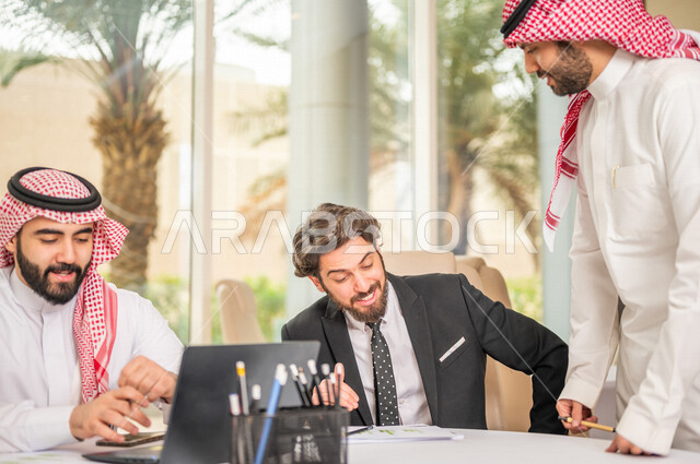 A Saudi Arabian Gulf team in a business meeting with a new client wearing a formal suit, using a laptop computer in developing work and solving problems, developing projects, studying and analyzing new projects, evaluating partnership work, partnership an