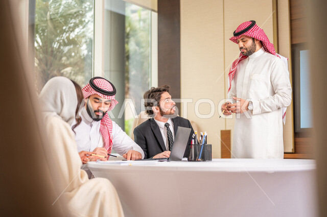 فريق عمل عربي خليجي سعودي في اجتماع عمل مع عميل جديد يرتدي البدلة الرسمية، استخدام الحاسوب المحمول في تطوير العمل وحل المشكلات، تطوير المشاريع، دراسة وتحليل المشاريع الجديدة، تقييم العمل الشراكي، الشراكة والتعاون، اجتماعات عمل، ورش عمل وتدريب