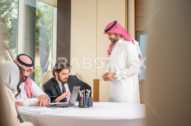 فريق عمل عربي خليجي سعودي في اجتماع عمل مع عميل جديد يرتدي البدلة الرسمية، استخدام الحاسوب المحمول في تطوير العمل وحل المشكلات، تطوير المشاريع، دراسة وتحليل المشاريع الجديدة، تقييم العمل الشراكي، الشراكة والتعاون، اجتماعات عمل، ورش عمل وتدريب