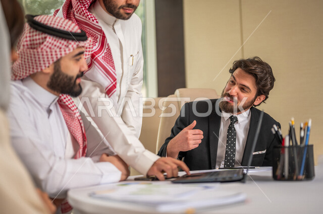 فريق عمل عربي خليجي سعودي في اجتماع عمل مع عميل جديد يرتدي البدلة الرسمية، استخدام الحاسوب المحمول في تطوير العمل وحل المشكلات، تطوير المشاريع، دراسة وتحليل المشاريع الجديدة، تقييم العمل الشراكي، الشراكة والتعاون، اجتماعات عمل، ورش عمل وتدريب