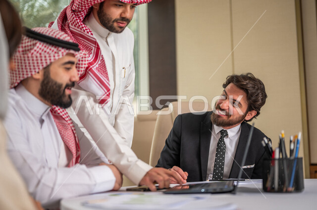 A Saudi Arabian Gulf team in a business meeting with a new client wearing a formal suit, using a laptop computer in developing work and solving problems, developing projects, studying and analyzing new projects, evaluating partnership work, partnership an