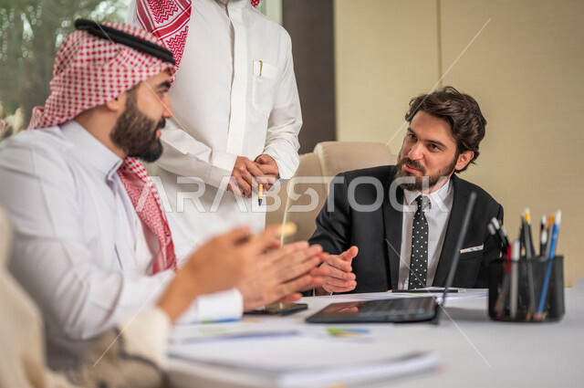 A Saudi Arabian Gulf team in a business meeting with a new client wearing a formal suit, using a laptop computer in developing work and solving problems, developing projects, studying and analyzing new projects, evaluating partnership work, partnership an