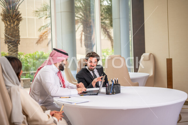 A Saudi Arabian Gulf team in a business meeting with a new client wearing a formal suit, using a laptop computer in developing work and solving problems, developing projects, studying and analyzing new projects, evaluating partnership work, partnership an