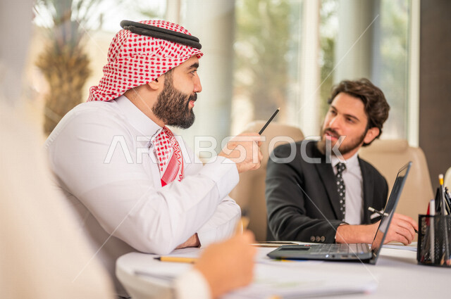 A Saudi Arabian Gulf team in a business meeting with a new client wearing a formal suit, using a laptop computer in developing work and solving problems, developing projects, studying and analyzing new projects, evaluating partnership work, partnership an