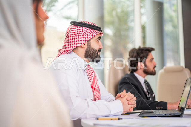 A Saudi Arabian Gulf team in a business meeting with a new client wearing a formal suit, using a laptop computer in developing work and solving problems, developing projects, studying and analyzing new projects, evaluating partnership work, partnership an