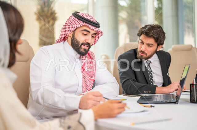 A Saudi Arabian Gulf businessman in the traditional Saudi dress in a business meeting with a new client wearing a formal suit, a Saudi Arabian Gulf business woman working on the study and analysis of new projects, the use of a laptop in business developme