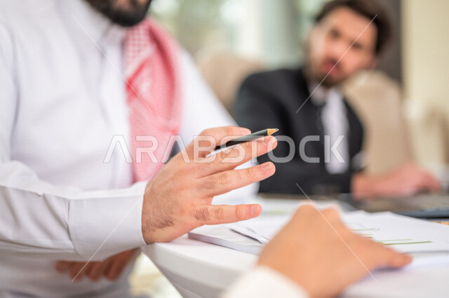 A Saudi Arabian Gulf businessman in the traditional Saudi dress in a business meeting with a new client wearing a formal suit, using a laptop computer in work development and problem solving, business meetings, project development, study and analysis of n