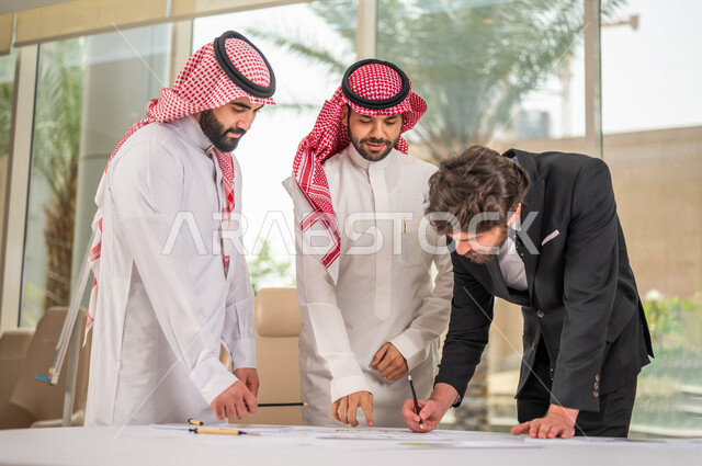 رجل اعمال عربي سعودي خليجي بالثوب السعودي التقليدي يقوم بتوقيع اتفاقية عمل لمشروع جديد مع عميل يرتدي البدلة الرسمية، رجل اعمال خليجي يشارك في نجاح صفقات العمل، التحقق والتدقيق في شروط العقد، قراءة البنود الخاصة بالعقد، الموافقة على الشروط، توقيع العقود