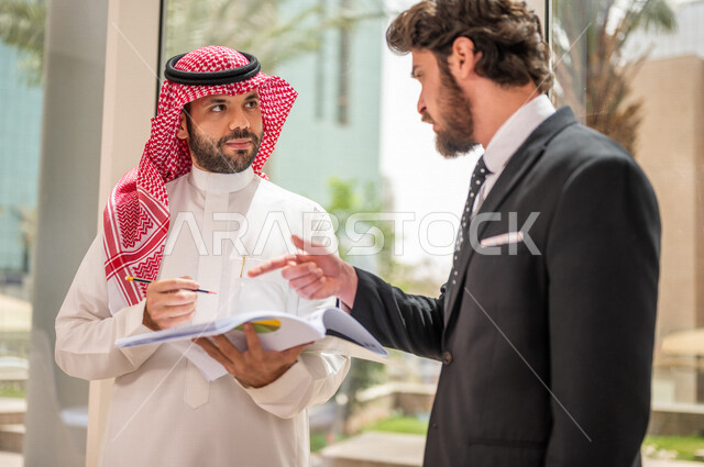 رجل اعمال عربي سعودي خليجي بالثوب السعودي التقليدي يتناقش مع عميل يرتدي البدلة الرسمية، اتفاقية عمل لمشروع جديد، تحليل وتخطيط المشاريع، تطوير العمل وحل المشكلات، الوحدة والعمل الجماعي، تحقيق اهداف الشركه