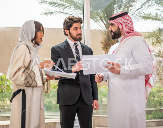 رجل اعمال عربي سعودي خليجي بالثوب السعودي التقليدي يتناقش مع عميل يرتدي البدلة الرسمية، اتفاقية عمل لمشروع جديد، سيدة اعمال عربية سعودية خليجية تعمل على تحليل وتخطيط المشاريع، تطوير العمل وحل المشكلات، الوحدة والعمل الجماعي، تحقيق اهداف الشركه 