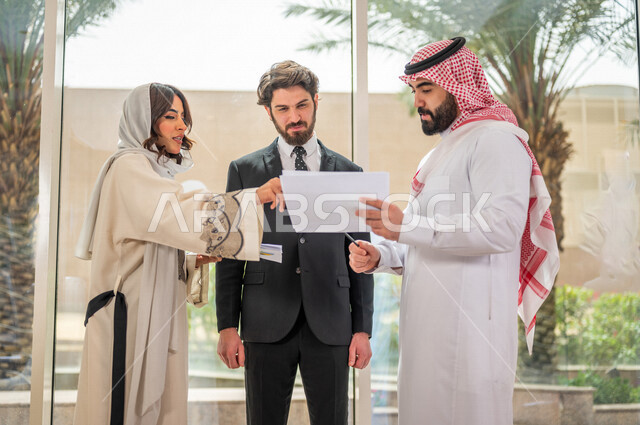رجل اعمال عربي سعودي خليجي بالثوب السعودي التقليدي يتناقش مع عميل يرتدي البدلة الرسمية، اتفاقية عمل لمشروع جديد، سيدة اعمال عربية سعودية خليجية تعمل على تحليل وتخطيط المشاريع، تطوير العمل وحل المشكلات، الوحدة والعمل الجماعي، تحقيق اهداف الشركه 