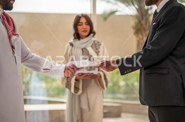 رجل اعمال عربي سعودي خليجي بالثوب السعودي التقليدي يتناقش مع عميل يرتدي البدلة الرسمية، اتفاقية عمل لمشروع جديد، سيدة اعمال عربية سعودية خليجية تعمل على تحليل وتخطيط المشاريع، تطوير العمل وحل المشكلات، الوحدة والعمل الجماعي، تحقيق اهداف الشركه 