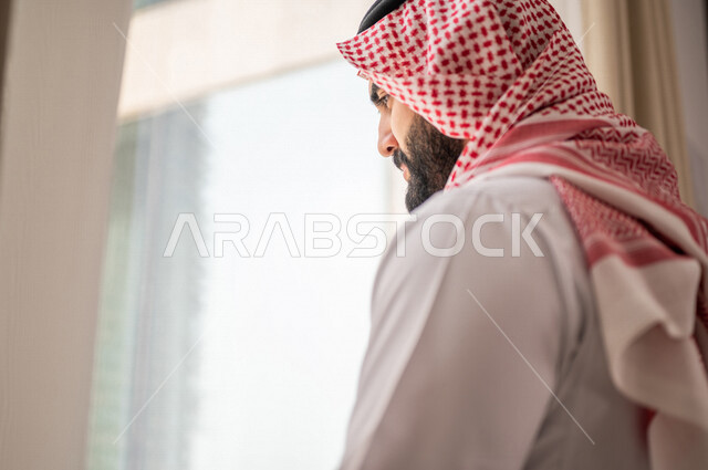 رجل عربي خليجي سعودي يقف امام النافذة، غرفة فندقية، النظر الى الخارج من خلال النافذة، إشراقة يوم جديد، مفهوم الهمة والنشاط، التخخطيط المستقبلي، الرؤية المستقبلية، سياحة وفندقة