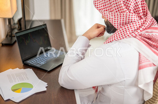 رجل عربي خليجي سعودي يقوم بتحليل البيانات على الحاسوب المحمول، متابعة مخطط الرسم البياني، تدقيق وتحليل بيانات المشروع، دراسة مشاريع جديدة، صعود وهبوط البورصة، النمو الاقتصادي، الاستثمار المالي
