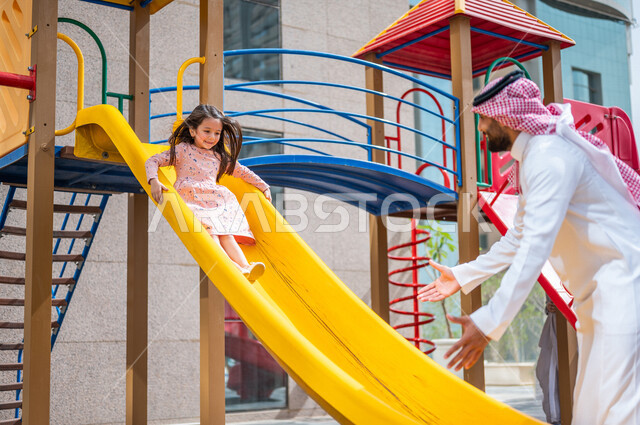 طفلة عربية خليجية سعودية مستمتعة بالتزحلق على الزحليقة ، رجل خليجي سعودي يشاهد ابنته اثناء اللعب بالالعاب الترفيهية ،التسلية والترفيه ،اجواء صيفية ممتعة ، رحلة سياحية ترفيهية ، عطلة صيفية سعيدة 
