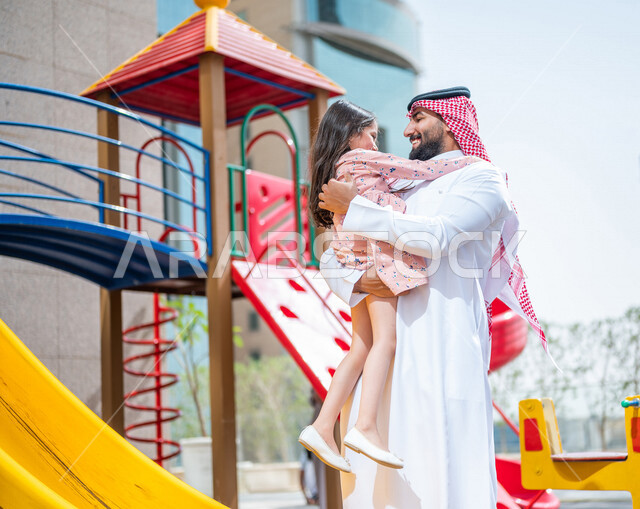 رجل عربي خليجي سعودي مستمتع بقضاء وقت ممتع مع ابنته في احدا الحدائق في المملكة العربية السعودية  ، التسلية والترفيه ، اجواء صيفية ممتعة ، قضاء وقت عائلي ممتع، عطلة صيفية سعيدة