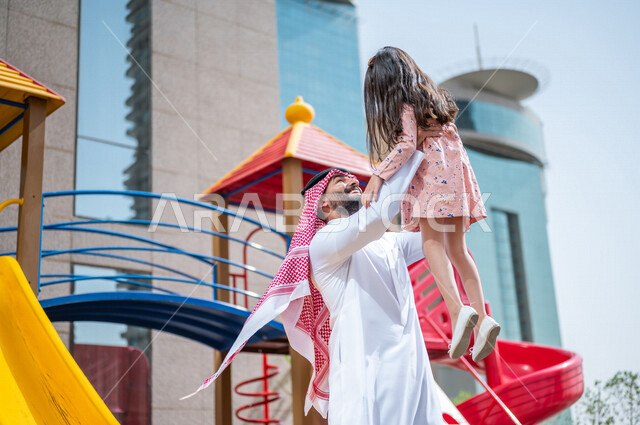 رجل عربي خليجي سعودي مستمتع بقضاء وقت ممتع مع ابنته في احدا الحدائق في المملكة العربية السعودية  ، التسلية والترفيه ، اجواء صيفية ممتعة ، قضاء وقت عائلي ممتع، عطلة صيفية سعيدة