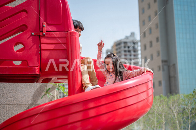 طفلان عربيان خليجيان سعوديان يستمتعان باللعب على لعبة التزحلق في احدى الحدائق العامة في المملكة العربية السعودية ،التسلية والترفيه ،مشاركة الاطفال بالانشطة الترفيهية ، عطلة صيفية سعيدة 