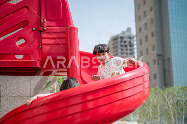 طفلان عربيان خليجيان سعوديان يستمتعان باللعب على لعبة التزحلق في احدى الحدائق العامة في المملكة العربية السعودية ،التسلية والترفيه ،مشاركة الاطفال بالانشطة الترفيهية ، عطلة صيفية سعيدة 
